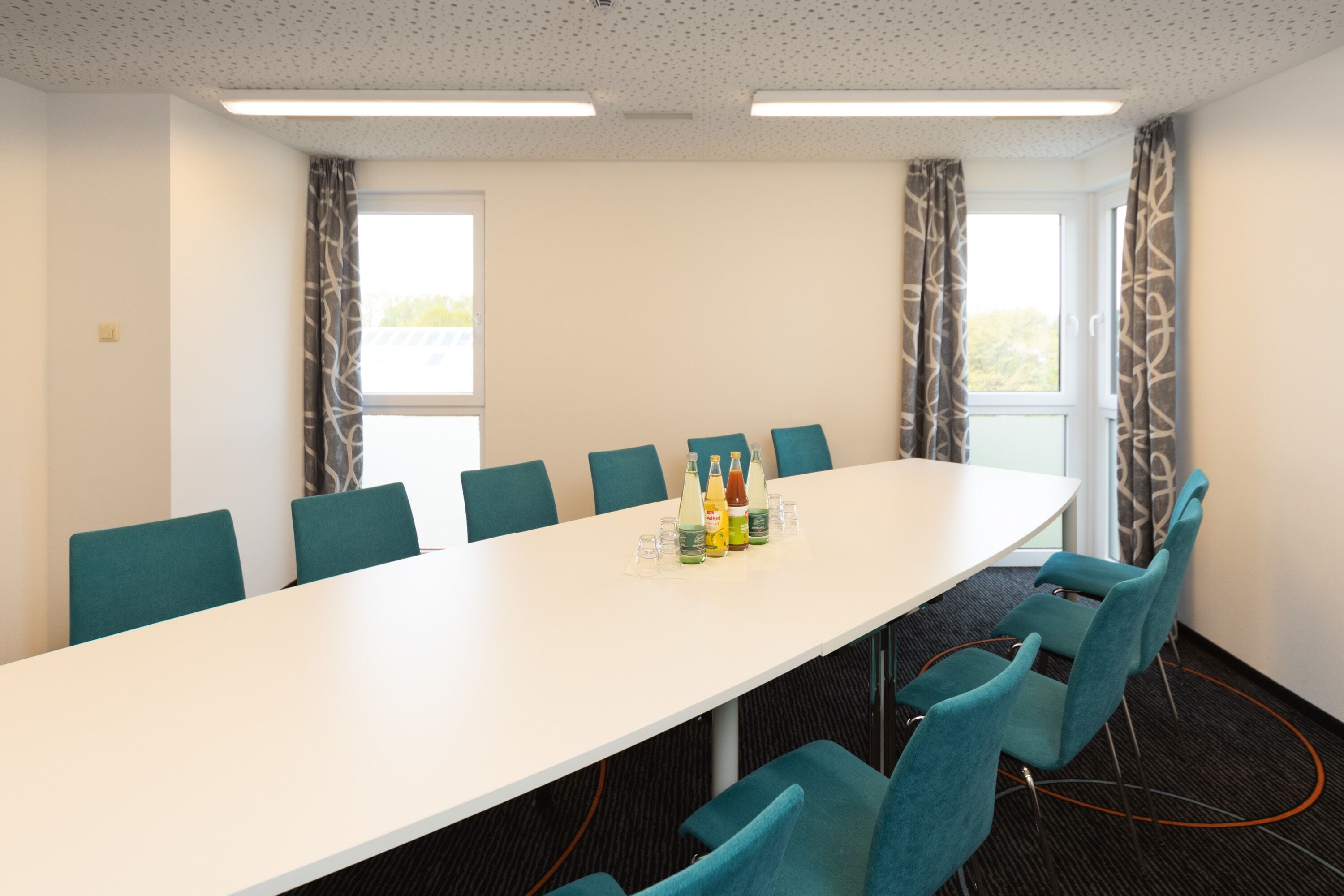 A conference room with a long white table, teal chairs, and a bottle arrangement on the table.