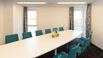 A conference room with a long white table, teal chairs, and a bottle arrangement on the table.