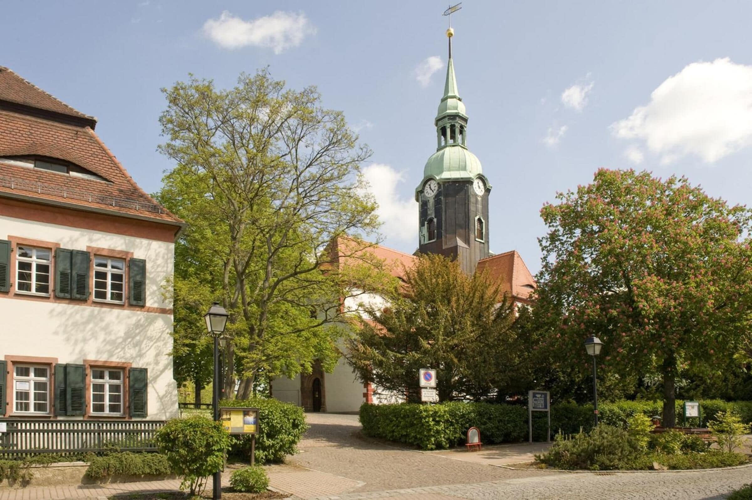 A church with a tall steeple and a clock tower, surrounded by trees and a cobblestone path.