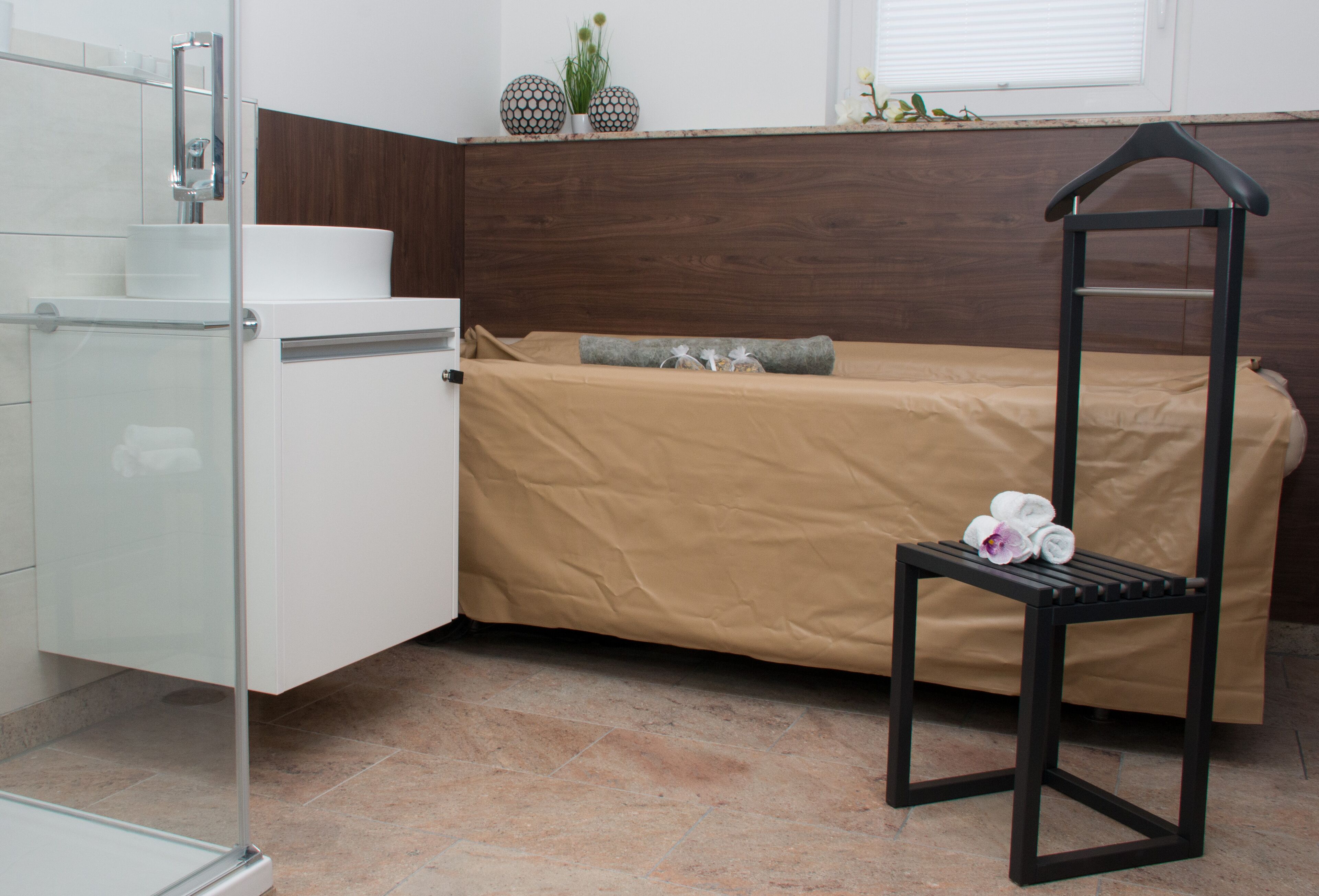 A compact bedroom with a bed, a small table, and a shower area.