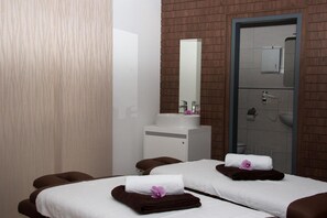 Un cuarto de spa con dos camillas de masaje, un lavamanos blanco y un espejo.