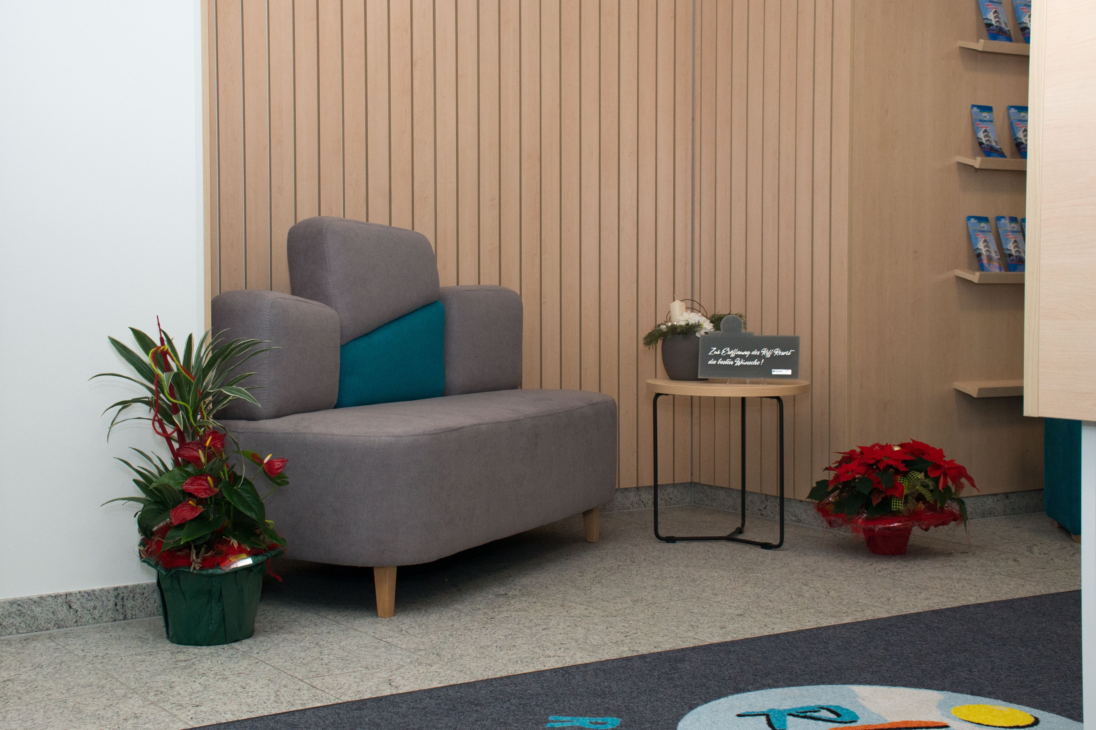 Een moderne wachtruimte met een grijze bank, een klein tafeltje met een bord en potplanten.