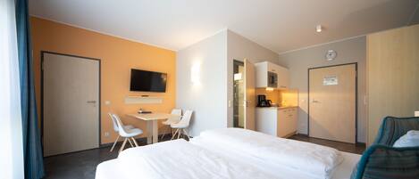 Habitación de hotel con una cama grande, un escritorio con sillas, un televisor y un kitchenette.