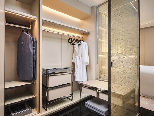 A modern bathroom with a walk-in shower, a vanity with a mirror, and a built-in storage unit with shelves and drawers.