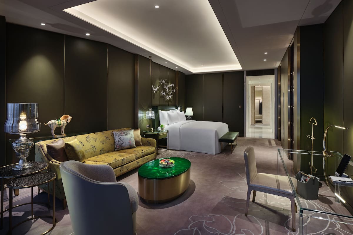 Moderni hotellihuone, jossa on sohva, pyöreä sohvapöytä, sänky ja työpöytä.
