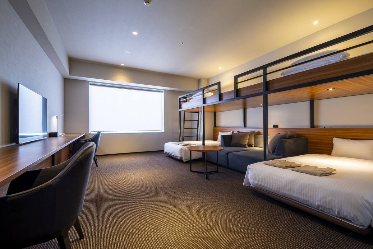 A hotel room with a bunk bed, a desk with a chair, a round table, and a sofa.