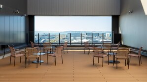 Eine Dachterrasse mit Korbmöbeln, Stühlen und Tischen, große Fenster mit Blick auf die Stadt.