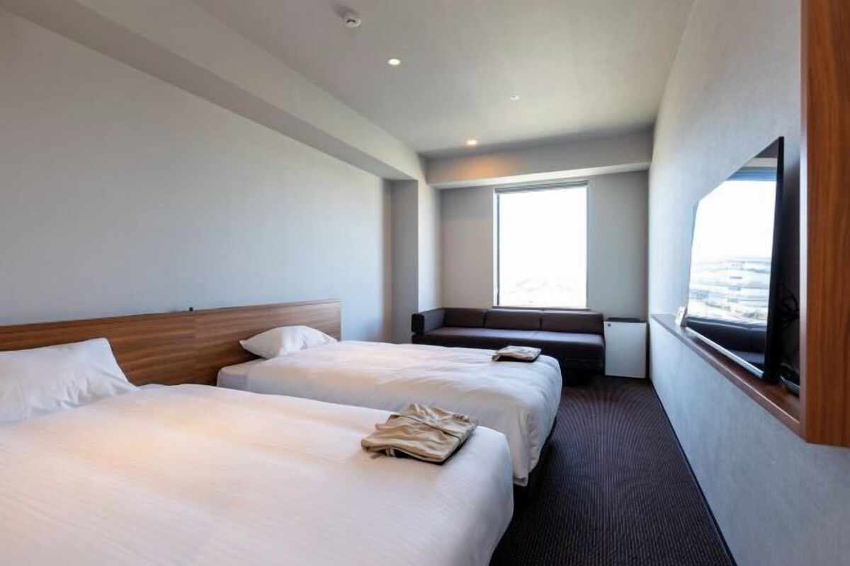 Une chambre d’hôtel avec deux lits, un coin salon et une grande fenêtre donnant sur un paysage agréable.