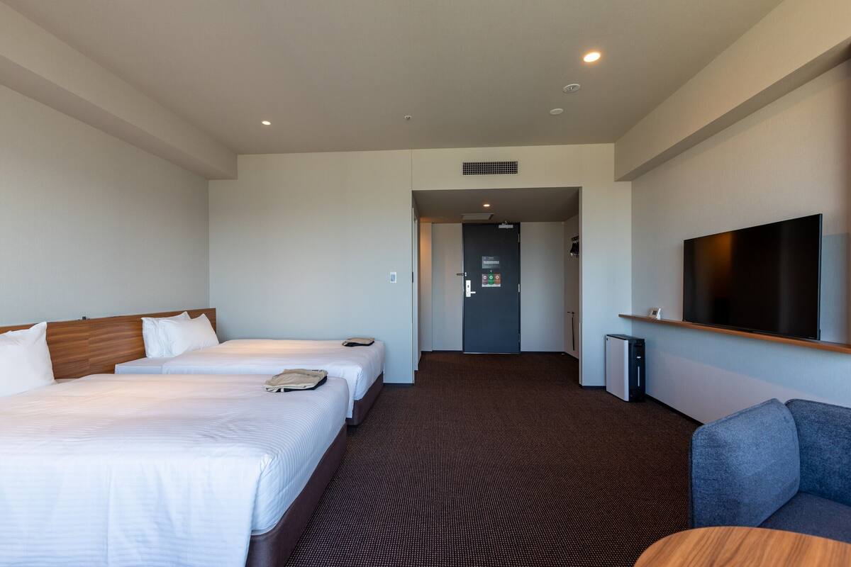 A hotel room with two beds, a TV, and a desk.