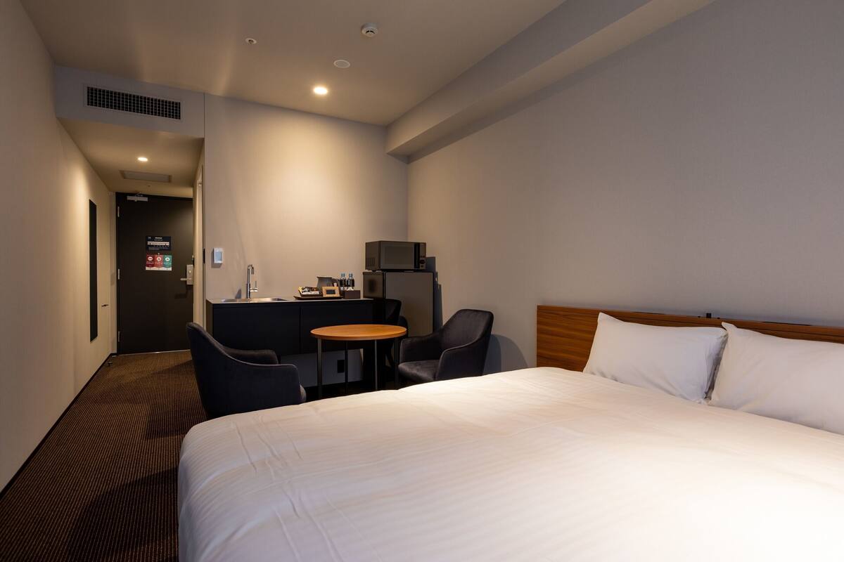 A hotel room with a large bed, a desk with a computer, a chair, and a small table.