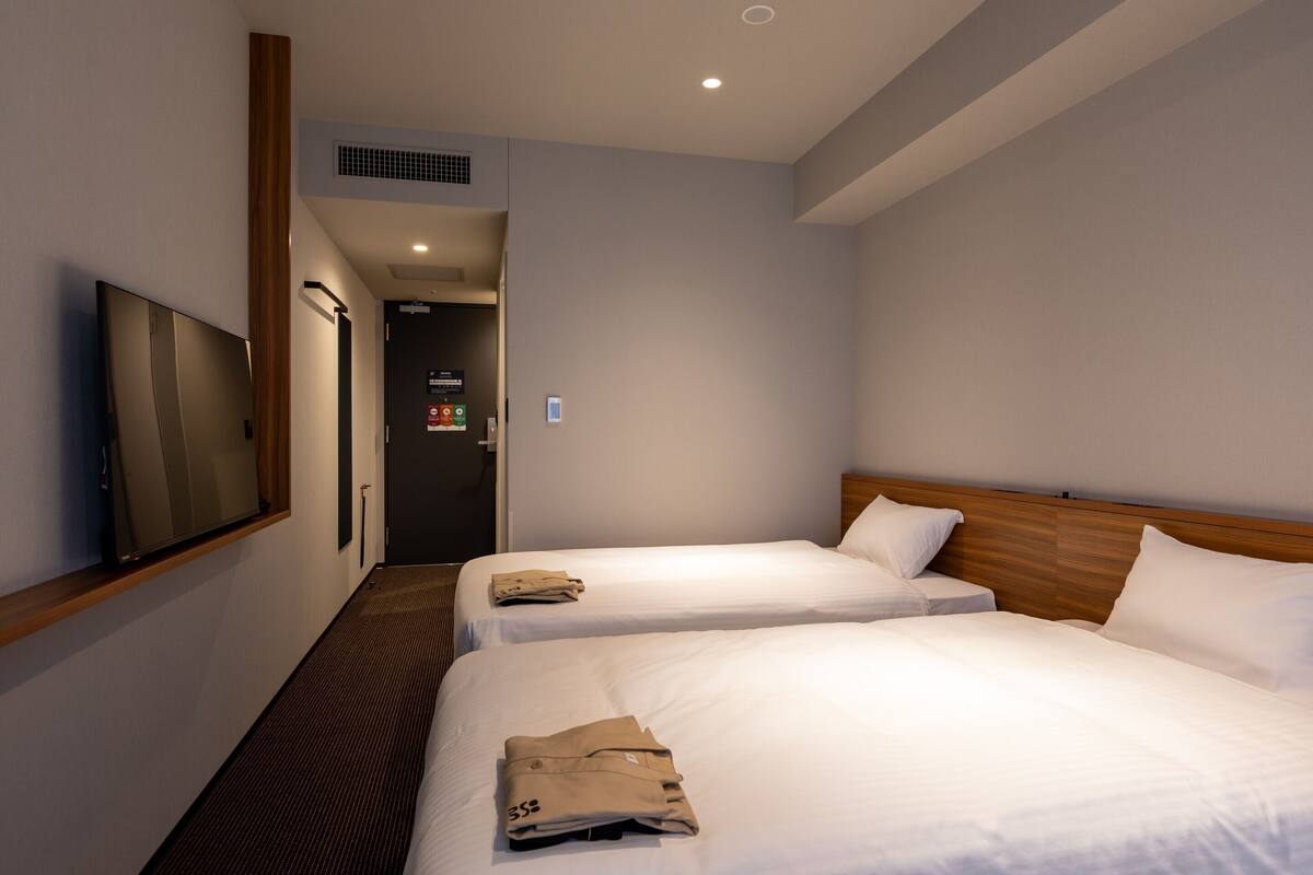 A hotel room with two beds, a TV mounted on the wall, and a door leading to a hallway.