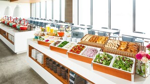 Ein Buffet mit verschiedenen Speisen und Getränken, präsentiert auf einer langen Theke mit Blick auf große Fenster im Hintergrund.