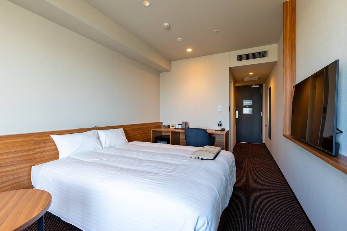 A hotel room with a large bed, a desk, a chair, and a TV mounted on the wall.