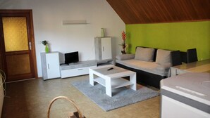 Una sala de estar moderna con techo inclinado, un sofá gris, una mesita de centro blanca y un mueble con televisor.