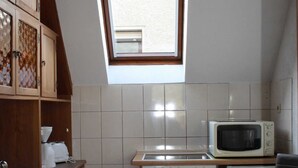 Una cocina compacta con armarios de madera, microondas, estufa y un ventanal sobre el fregadero.