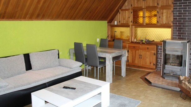 Una sala acogedora con sofá, mesa de comedor y sillas, una cocina con armarios de madera y pared de ladrillo, y un estufa de leña.