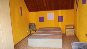 Una habitación con techo de madera, una cama con manta a rayas, una silla, una mesita de noche de madera y un armario.