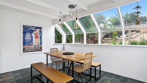 Ein Essbereich mit Holztisch und -stühlen, einer Bank, einem Poster an der Wand und Blick ins Freie durch große Fenster.