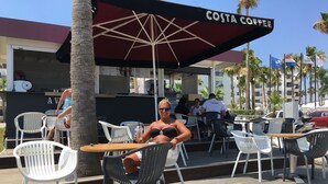 Outdoor seating with a Costa Coffee umbrella, white and black chairs, and a wooden deck. - Luxury Villa - Private Pool and Wifi Perfect Location for a Holiday! (Paralimni)