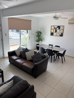 A modern living room with a leather sofa, dining table, chairs, and a ceiling fan. - Luxury Villa - Private Pool and Wifi Perfect Location for a Holiday! (Paralimni)