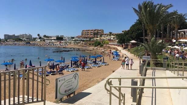 A beach with sun loungers and umbrellas, a sign indicating a wireless zone, and a building in the background. - Luxury Villa - Private Pool and Wifi Perfect Location for a Holiday! (Paralimni)