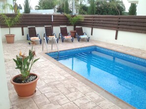 A swimming pool with lounge chairs and potted plants.