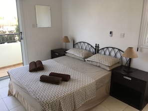 A bedroom with a bed, two nightstands, two lamps, and a view of the outside.