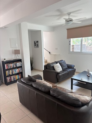 A modern living room with a sectional sofa, a coffee table, a bookshelf, and a ceiling fan. - Luxury Villa - Private Pool and Wifi Perfect Location for a Holiday! (Paralimni)