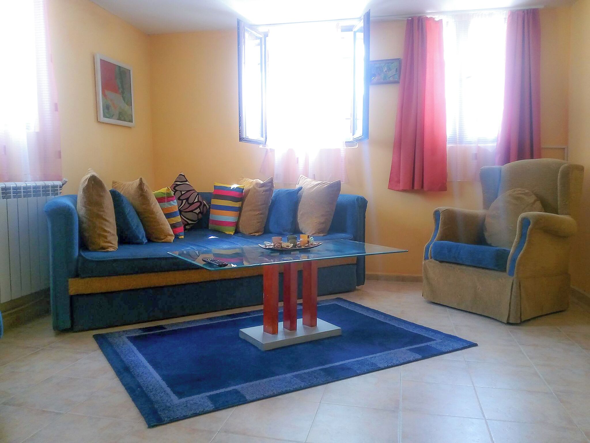 A living room with a blue sofa, a glass coffee table, and a beige armchair.