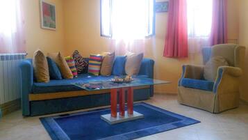 A living room with a blue sofa, a glass coffee table, and a beige armchair.