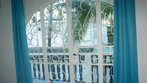 A room with a view through a metal gate to a balcony with a checkered floor and a palm tree. - House in Quiet Residence (Grand-Baie)