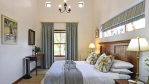 Quarto com cama, luminárias de cabeceira, mesa de cabeceira, cômoda, janela com cortinas, quadro e lustre.