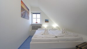 A bedroom with a bed, a window, a radiator, and a painting on the wall. - App. Reif für die Insel (Sylt)