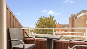 A balcony with wicker chairs and a table, overlooking a brick building and a tree. - App. Reif für die Insel (Sylt)