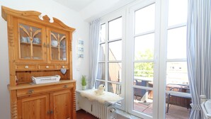 A room with a wooden cabinet, a radiator, and a large window with curtains. - App. Reif für die Insel (Sylt)