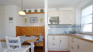 A compact kitchen with white cabinets, a wooden dining table, and a bench. - App. Reif für die Insel (Sylt)