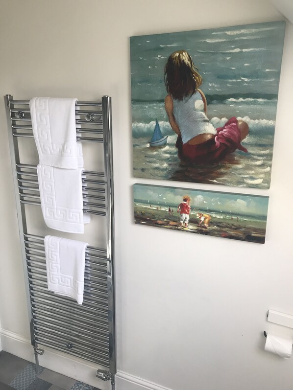 Un baño con un perchero que sostiene dos toallas, un cuadro de un niño jugando en la playa y un dispensador de papel higiénico en la pared.