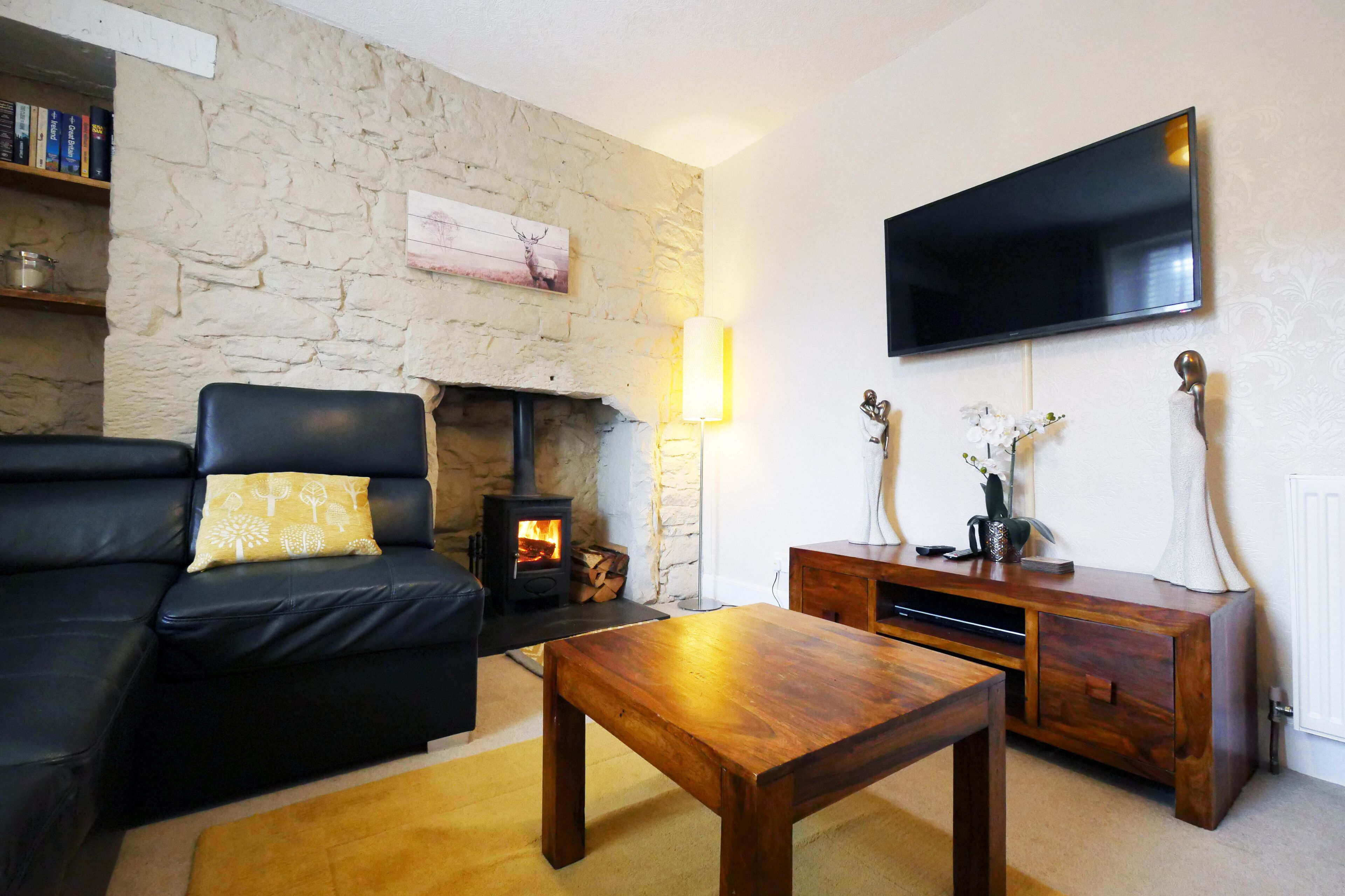 A living room with a stone wall, a black leather sofa, a wooden coffee table, a TV mounted on the wall, and a fireplace.