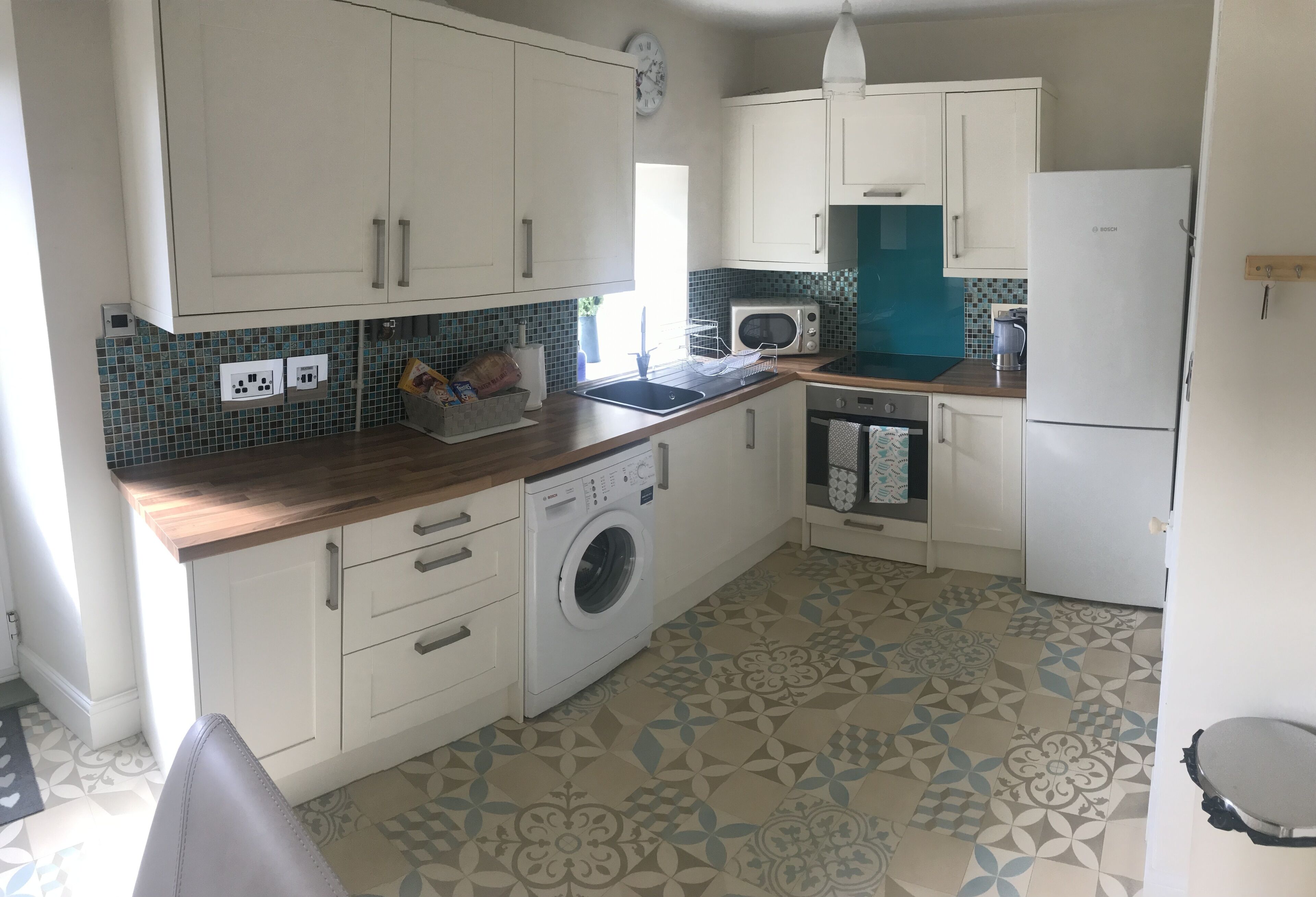 A compact kitchen with white cabinets, a washing machine, a microwave, and a refrigerator.