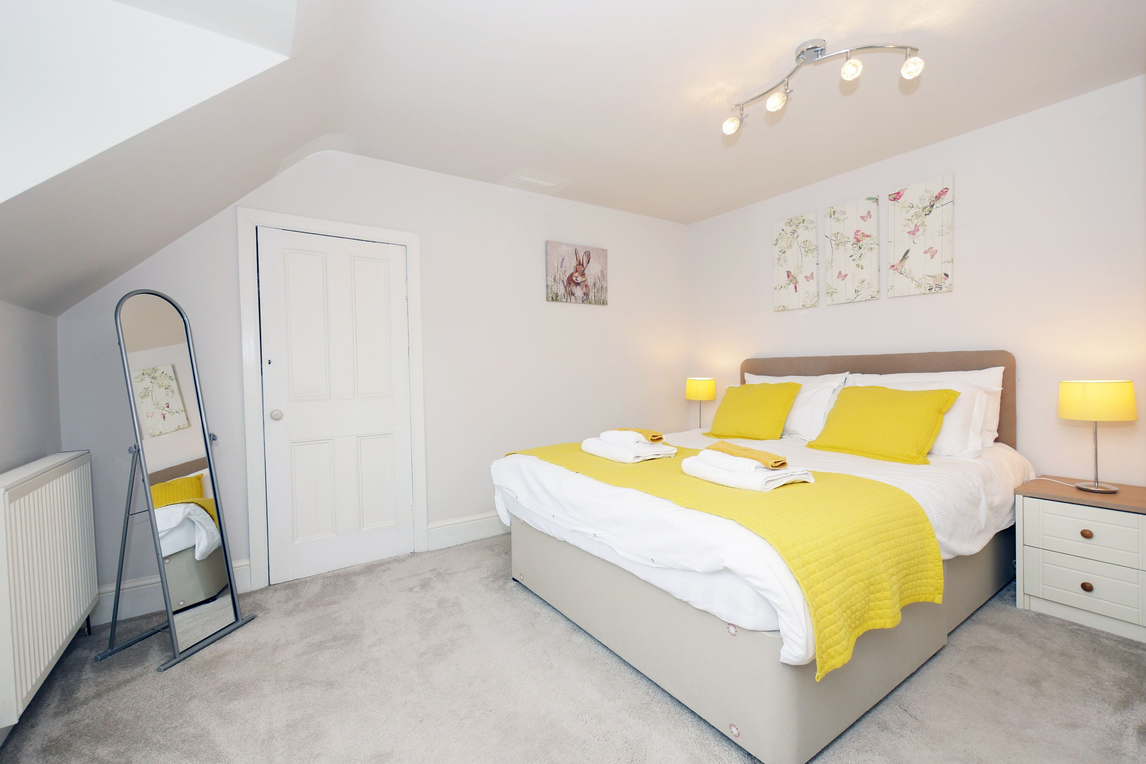Een slaapkamer met een bed, nachtkastjes, een spiegel en kunstwerken aan de muur.