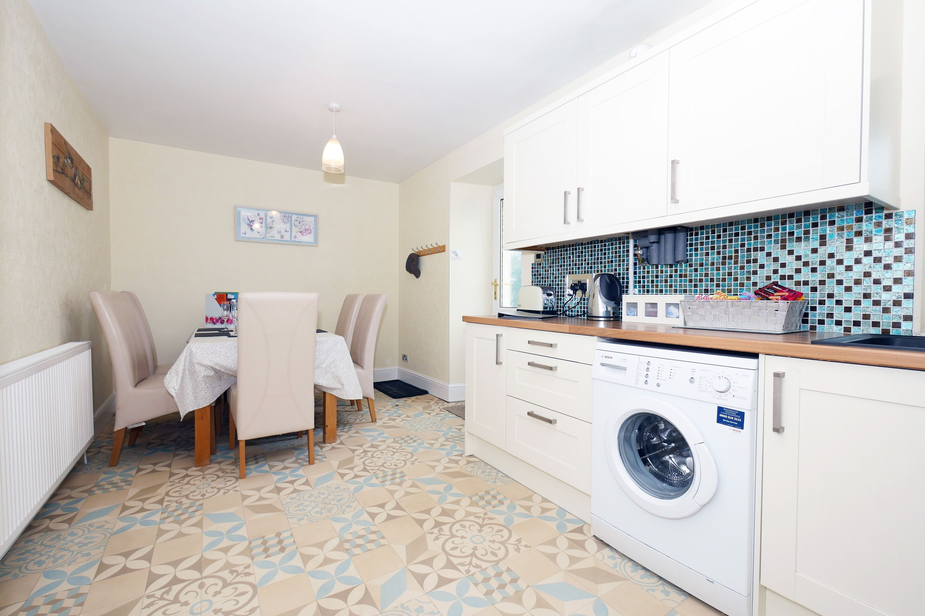 Une cuisine compacte équipée d’un lave-linge, d’un coin repas avec des chaises et d’un pare-feu en carrelage.