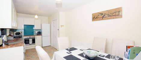 A compact kitchen with modern appliances, a dining area with a table set for two, and a wall-mounted artwork.