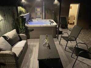 An outdoor patio with a hot tub, wicker furniture, and a table with a bottle. - Ardentorrie Holiday Home (Inverness)