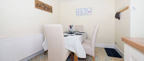 Zona pranzo con tavolo imbandito per due persone, due sedie, un appendiabiti a parete e un termosifone.