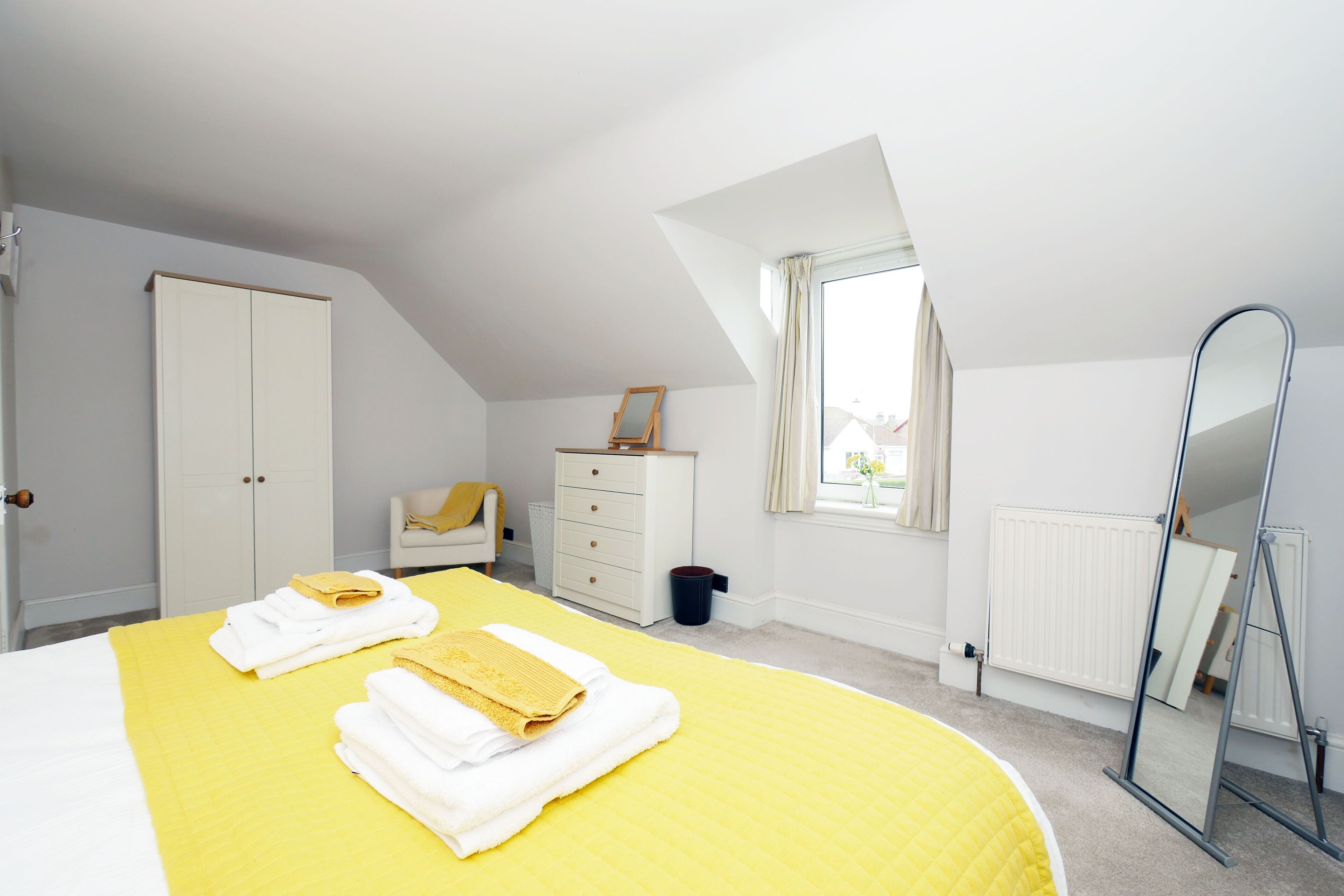 Une chambre à coucher avec un lit, une commode, un miroir et une fenêtre.