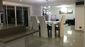 Ein moderner Essbereich mit Glastrennwand, einer Chandelierleuchtre und einem Flachbildfernseher an der Wand.