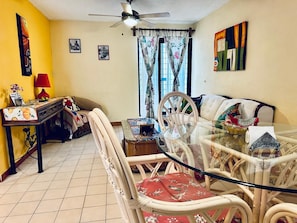A living room with a glass-top dining table, wicker chairs, a sofa, a red lamp, and a ceiling fan. - Nice Apartment, Equipped Near the Malecon and the Beach (La Paz)