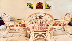 A dining area with wicker chairs and a table, a tiled floor, and wall art depicting fruits. - Nice Apartment, Equipped Near the Malecon and the Beach (La Paz)