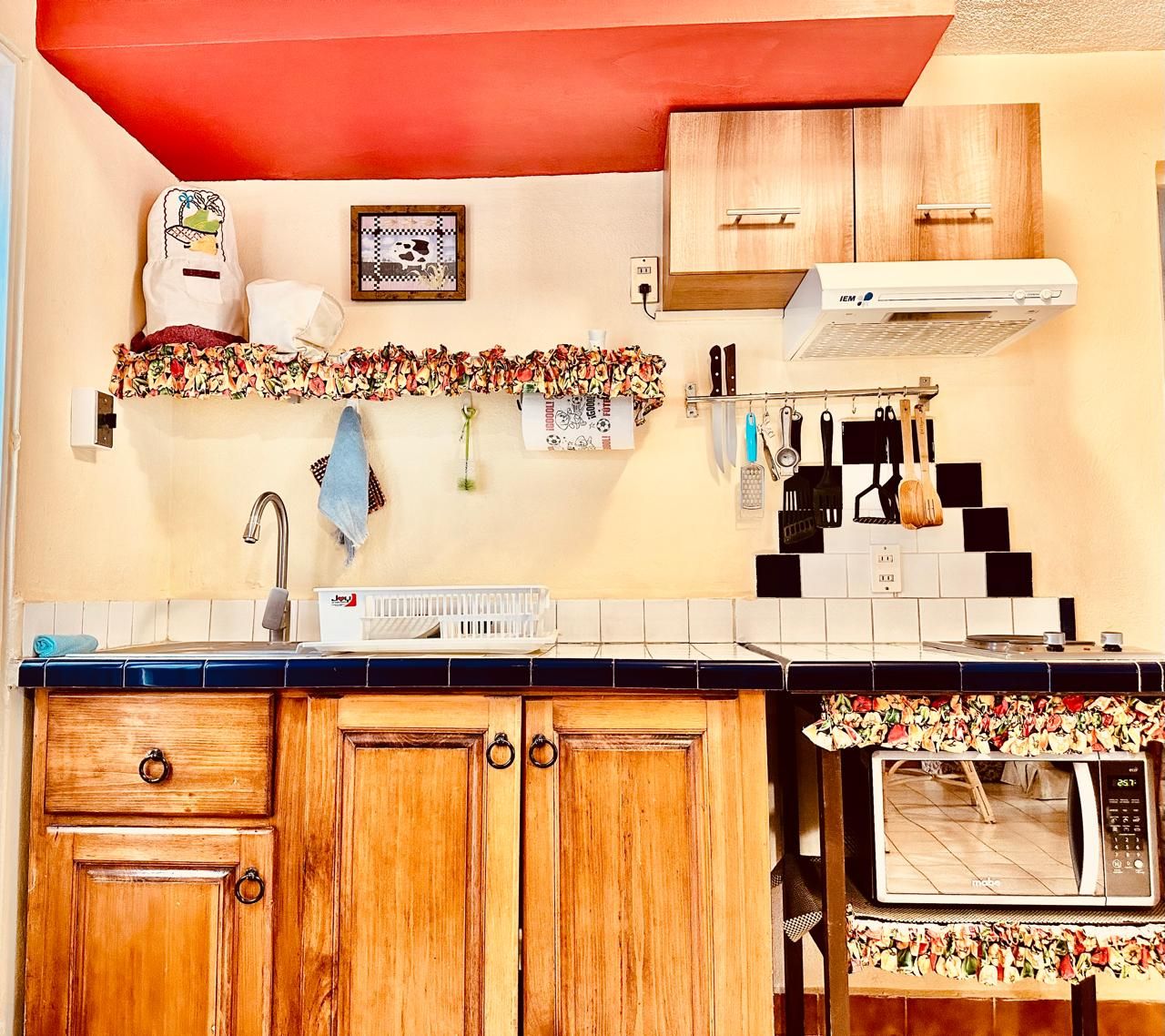 A kitchen with wooden cabinets, a microwave, a sink, and various kitchen utensils.