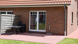 A brick building with a tiled roof, a sliding glass door, and a small patio area with a bench and chairs.